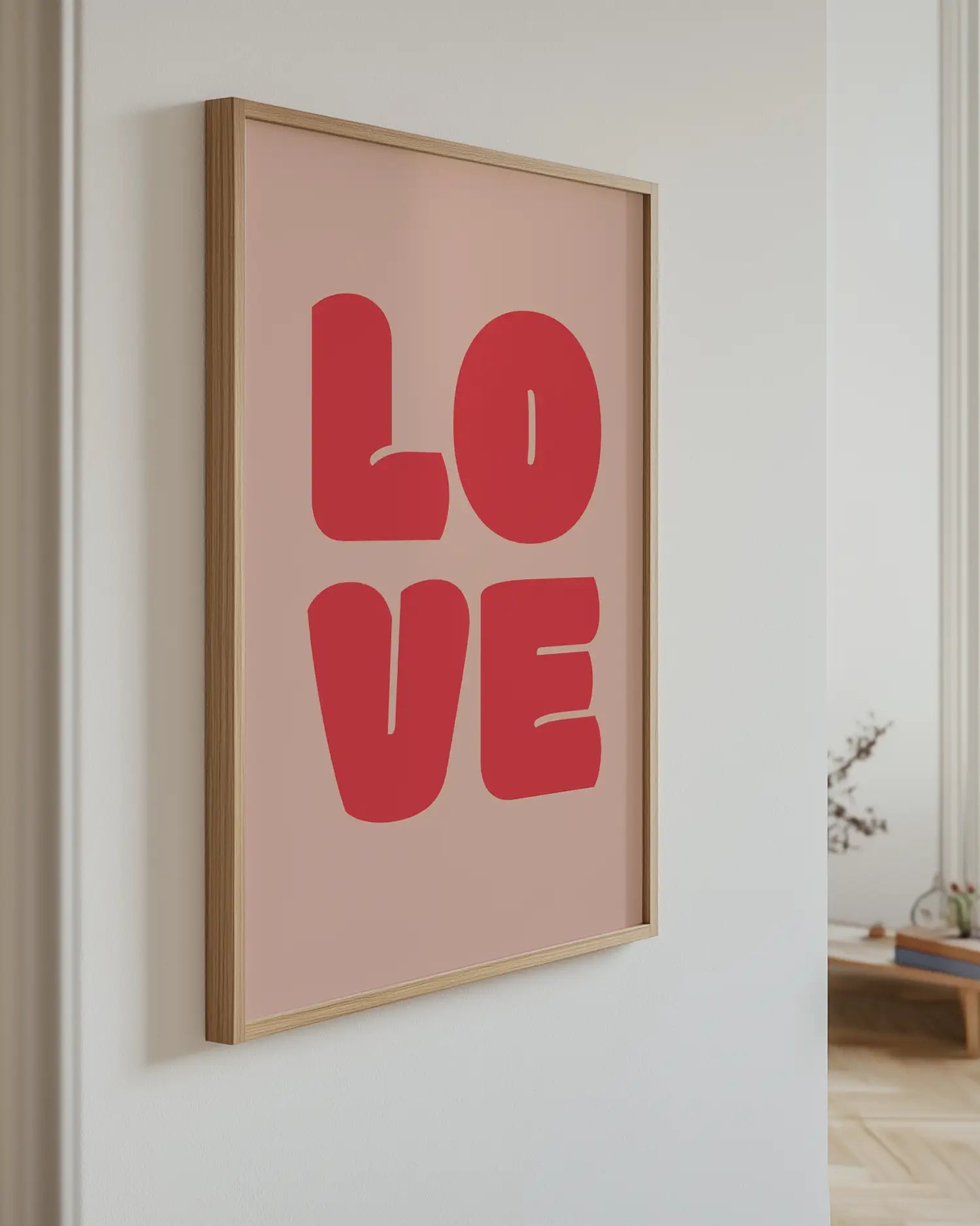 Framed artwork with 'LOVE' in red letters on a light pink background, hanging on a wall.