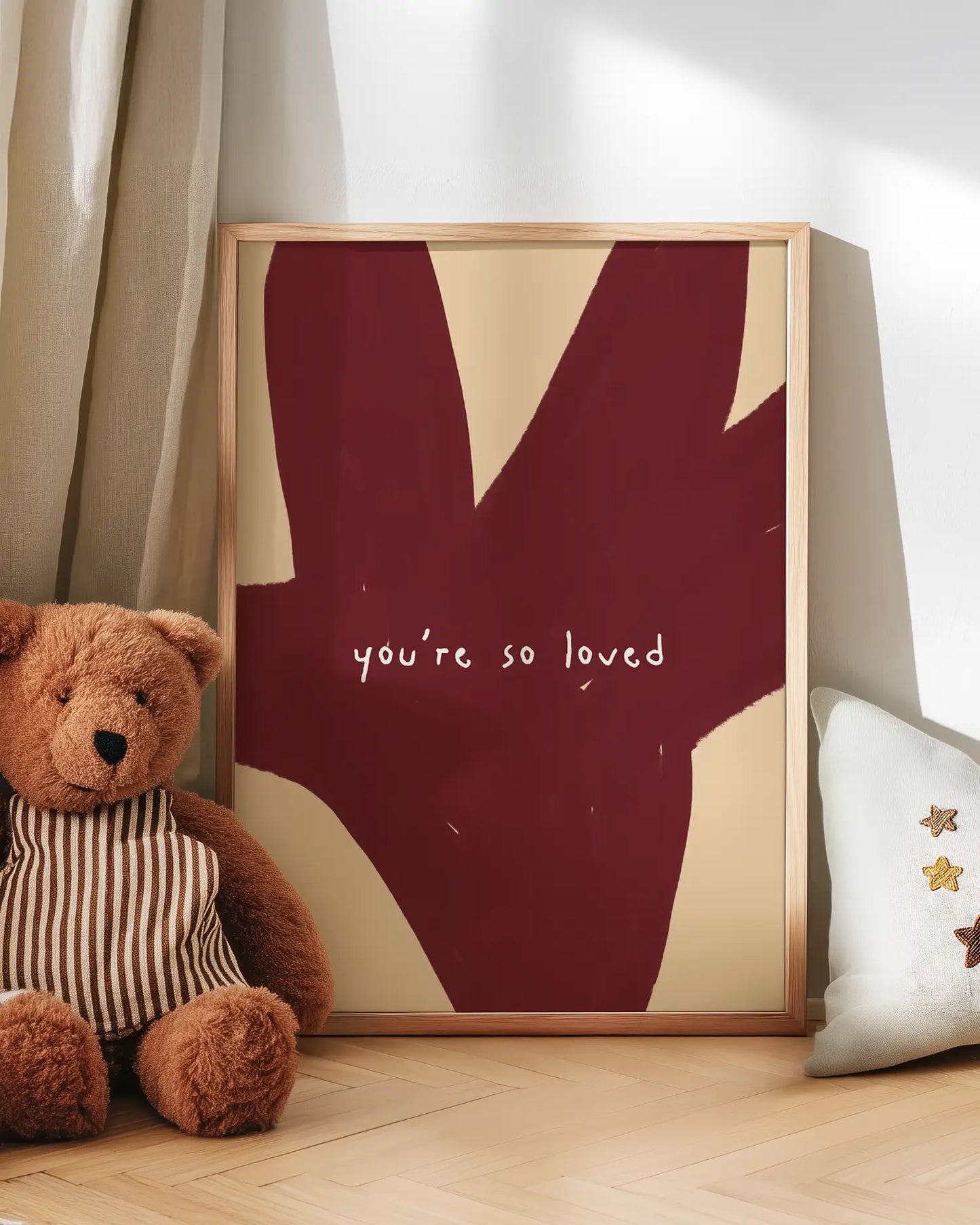 Framed artwork with 'you're so loved' text next to a teddy bear on a wooden floor.