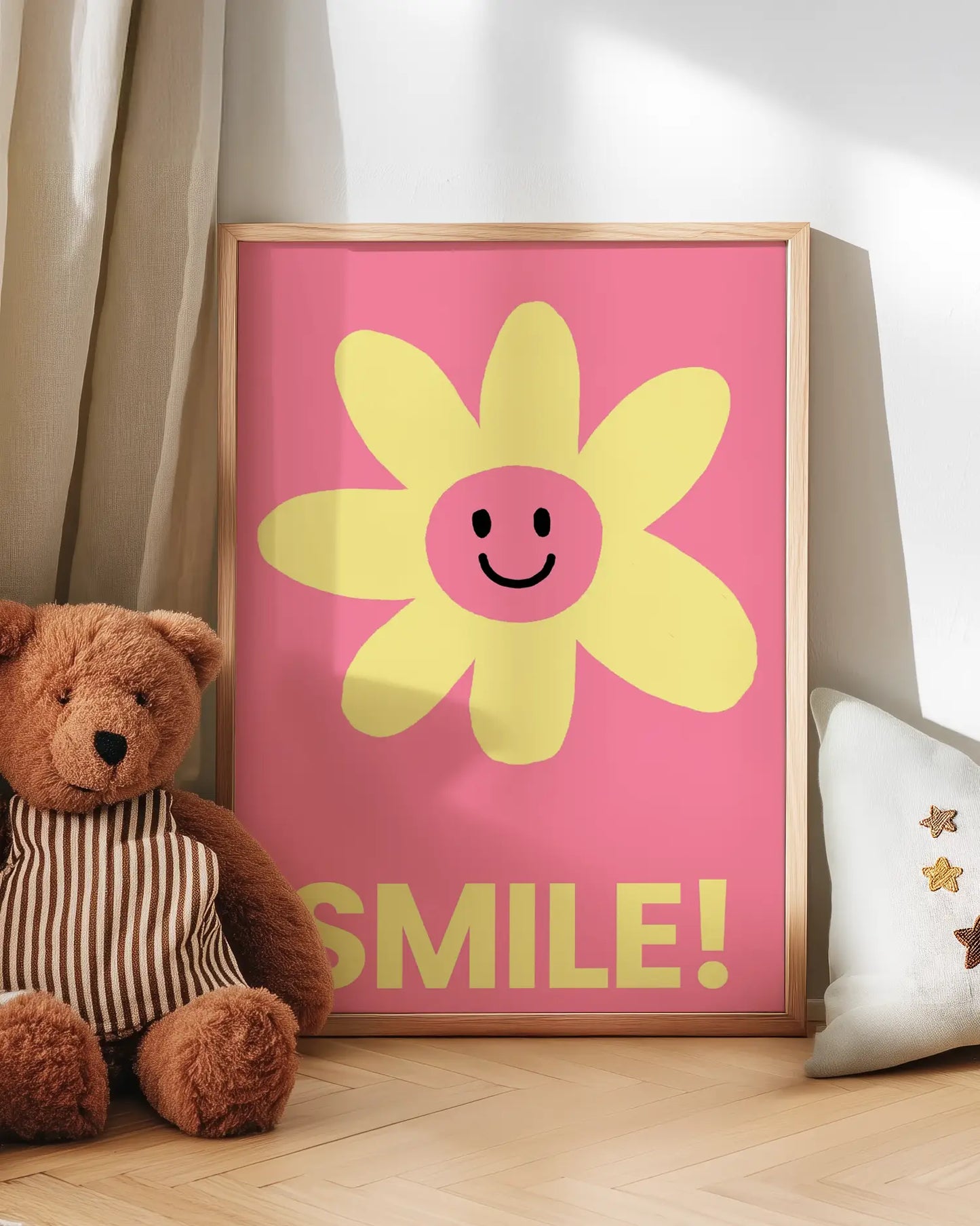 Framed pink poster with a yellow flower and 'SMILE!' text next to a teddy bear on a wooden floor.