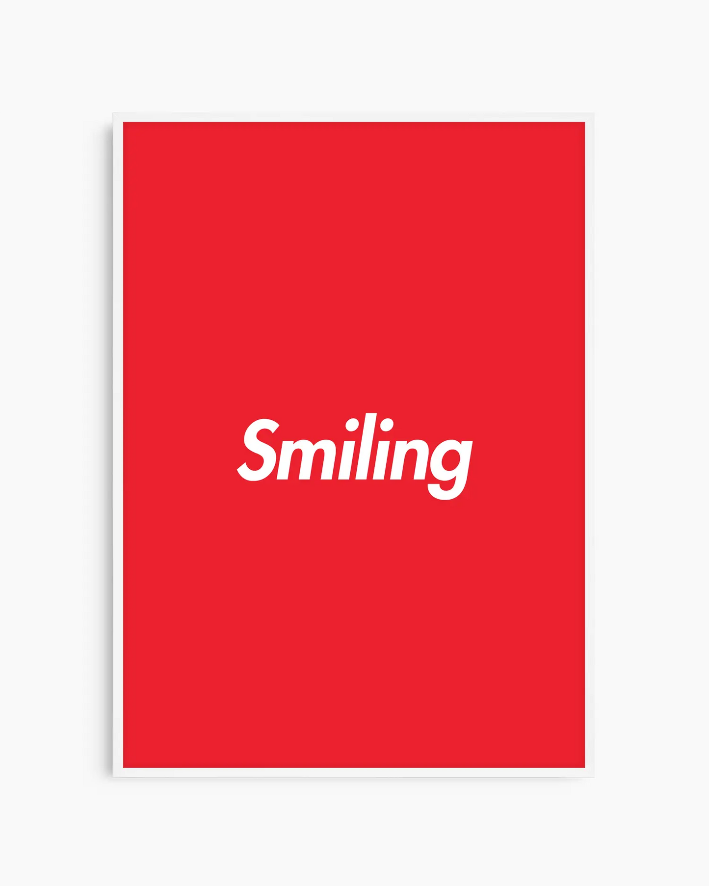 Red poster with 'Smiling' written in white, inserted in a white wooden frame.