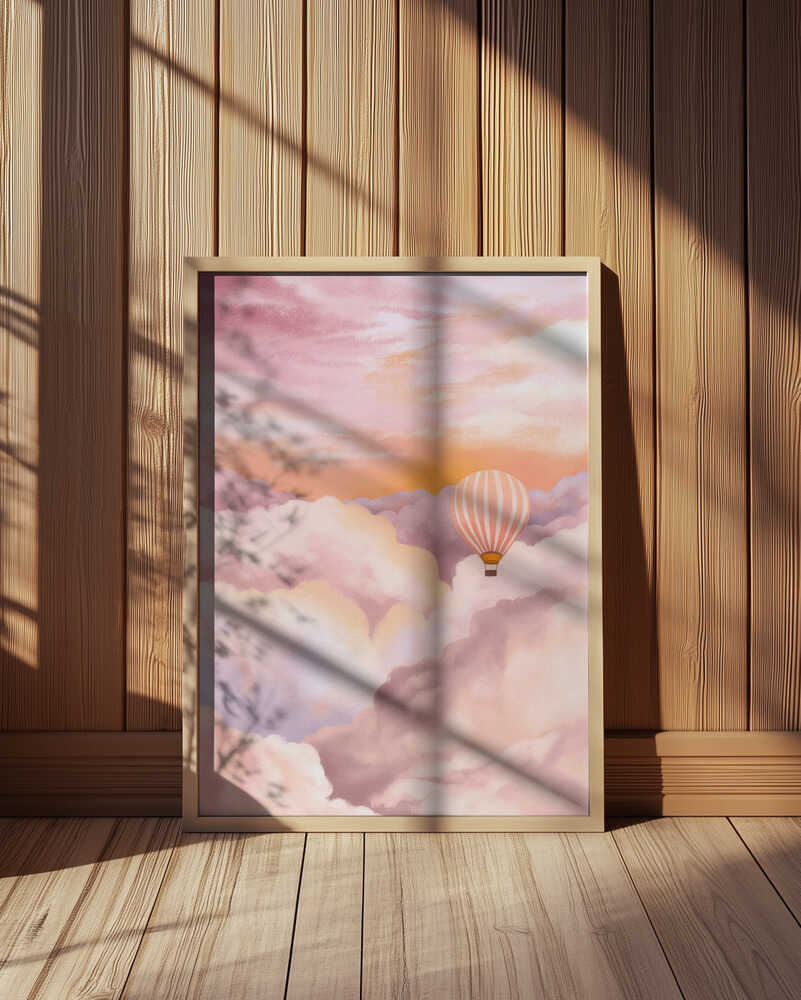 Dreamy hot air balloon art print featuring soft pastel clouds in shades of pink, purple, and orange. Displayed in a light wooden frame leaning against a wooden wall, illuminated by warm sunlight and shadows. Perfect wall art for modern Scandinavian or boho interiors.